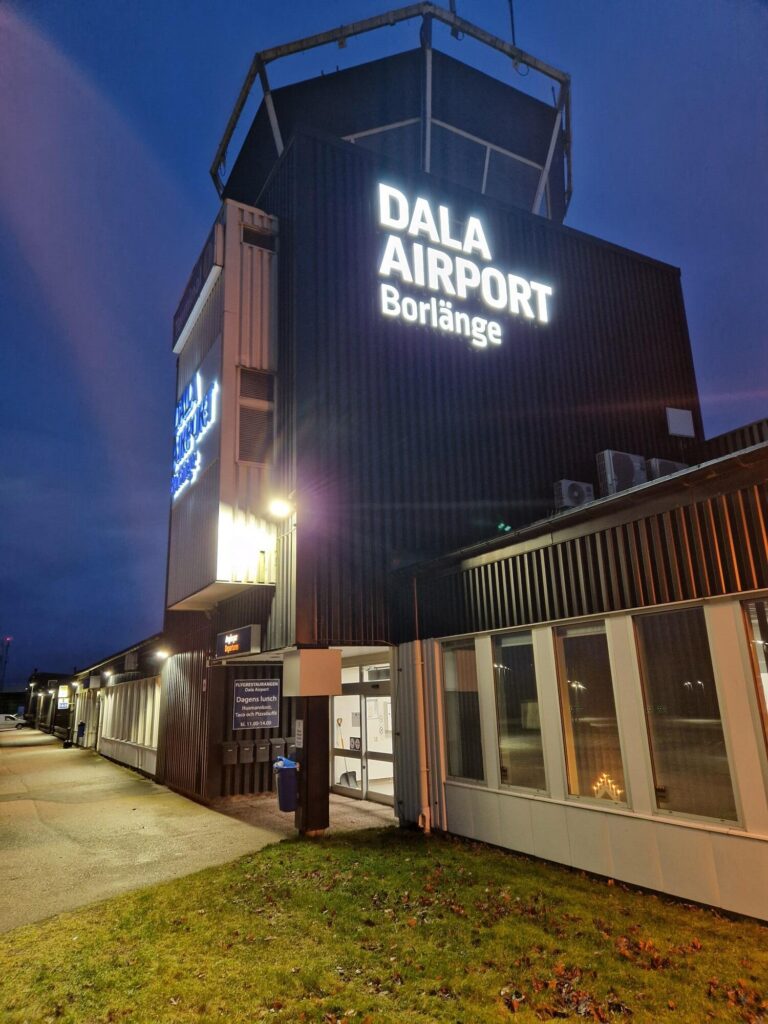 Dala Airports terminalbyggnad i Borlänge i skymning med belyst fasadskylt
