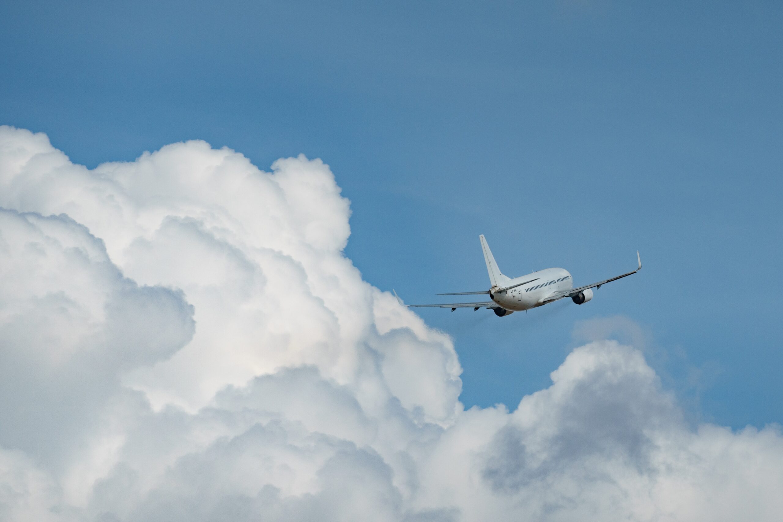 Vitt passagerarflygplan som flyger upp mot en blå himmel med vita moln