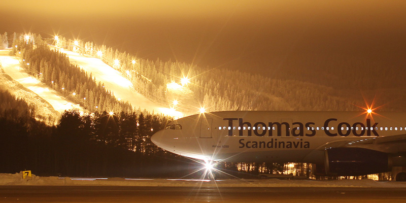 Thomas Cook-passagerarflygplan parkerat nattetid vid Dala Airport med belyst skidbacke i bakgrunden