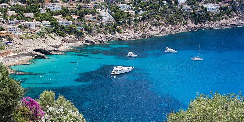 Vy över en badvik med turkost vatten och ankrade båtar på Rhodos